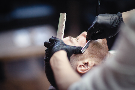 Hairdresser in black gloves shaves the razor's beard of the clientの写真素材