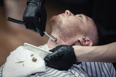 Hairdresser in black gloves shaves the razor's beard of the clientの写真素材