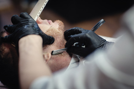 Hairdresser in black gloves shaves the razor's beard of the clientの写真素材