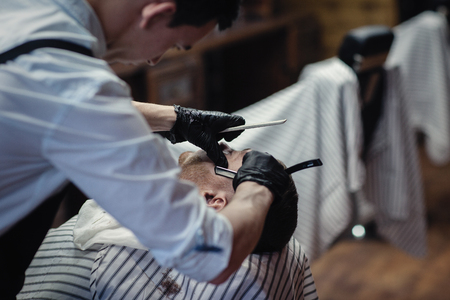 Hairdresser in black gloves shaves the razor's beard of the clientの写真素材