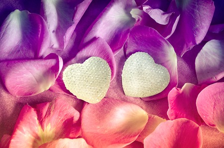 Background texture of beautiful delicate pink rose petals in a random pile and two hearts. The concept of love and romance. Valentines Day decoration.の写真素材