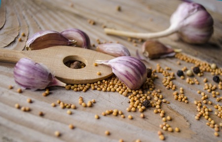 Cloves of garlic, mustard seeds and spoon on wooden board. Rustic style garlic on vintage wooden background. Fresh garlic clove. Garlic bulbs.の写真素材