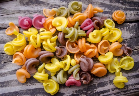 Heap of colored italian pasta on old woden desk. Bunch of raw pasta isolated on gray striped background.の写真素材