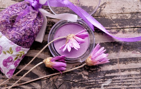 Purple eye shadow, surrounded by flowers and a package of lavender on dark textured wooden background. Fashion and make up theme.の写真素材