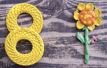 8 March symbol and handmade plasticine flower on wooden background. Happy woman's day design. Can be used as a decorative greeting card or postcard for international Woman's Day on 8 March.の写真素材