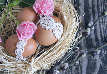 Nest with decorated eggs, roses and willow twigs on vintage wooden background. Spring Easter holiday arrangement.の写真素材