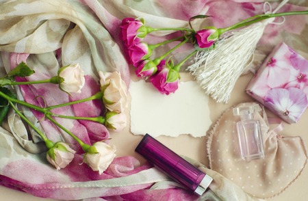 Photocomposition in a gentle vintage style in pastel colors. Tea pink roses lie on a silk scarf, surrounded by pearls, lipstick,perfume. Photo can be as a frame for the message to woman.Place for textの写真素材
