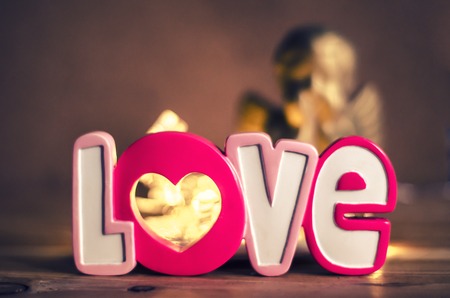 The inscription is love ceramic on a background of a backlit and a blurred golden angel. Valentine's Day Concept.の写真素材