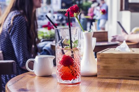 Photo mojito from strawberries. Red rose in a white vase in the background. Silhouetted by a girl.の写真素材