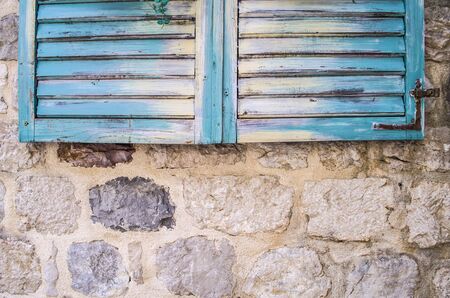 Old stone wall with closed weathered wooden shutters window.の写真素材