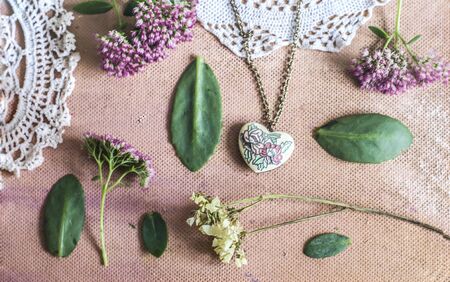 Sedum Spectabile and vintage brass pendant made of enamel hearts.Crocheted napkin on a pink...