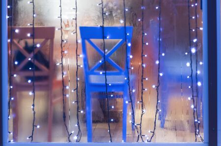 Colored chairs in the showcase of rain. Photo festive lights over glass.の写真素材