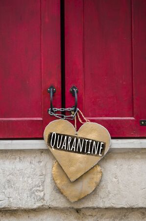 Inscription Quarantine on a wooden heart that hangs on red closed shutters. Quarantine closure of small business, concept photo.の写真素材