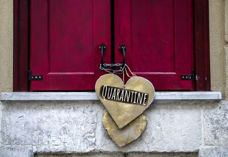 Inscription Quarantine on a wooden heart that hangs on red closed shutters. Quarantine closure of small business, concept photo.の写真素材