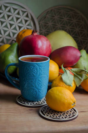 Fruits bergamot, pomegranate, lemon, pamelo, pear, tangerine, mango on a wooden background. Blue ceramic cup with rooibos tea.の写真素材