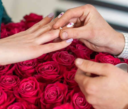 Betrothal ring on woman hand with pink bouqet of roses. Romantic event.