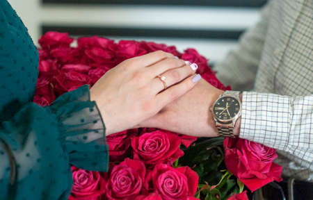 Betrothal ring on woman hand with pink bouqet of roses. Romantic event.の写真素材