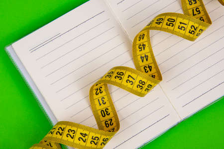 Yellow tape measure with paper note on green background