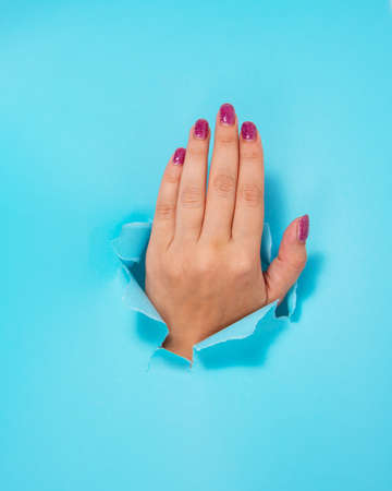 Woman hand in whole of torn blue paper backgroundの写真素材