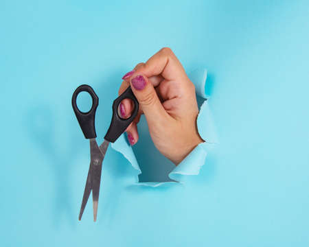Woman hand with scissors in whole of torn blue paper backgroundの写真素材