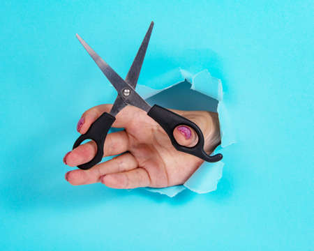 Woman hand with scissors in whole of torn blue paper backgroundの写真素材