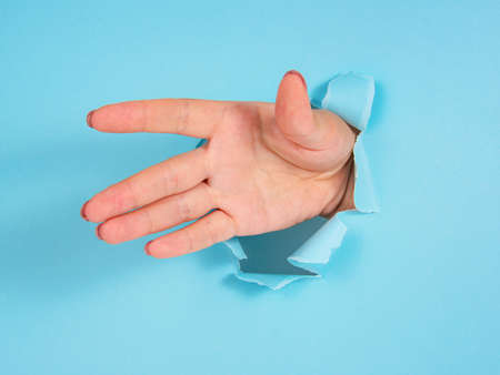 Woman hand in whole of torn blue paper backgroundの写真素材