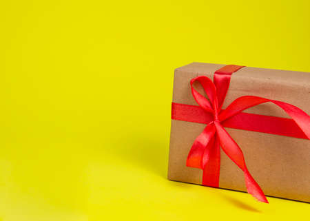 Craft gift box with red color bow on yellow background with copyspaceの写真素材
