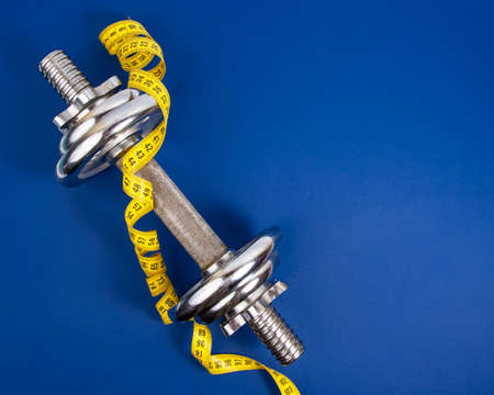 Stainless metal dumbbell and yellow tape measure on dark blue background with copyspace for textの写真素材