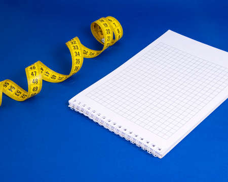 Yellow spiral tape measure and notebook on dark blue backgroundの写真素材