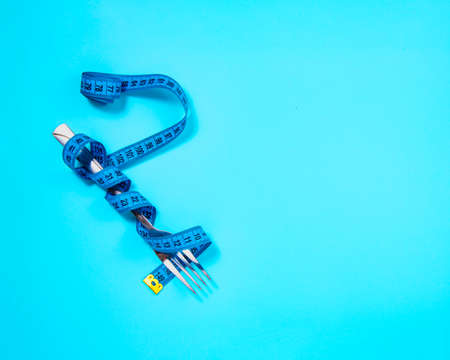 Metal fork and blue tape measure on blue background