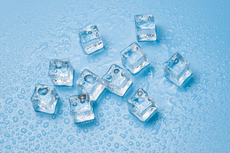 Ice cubes with water drops scattered on a blue background, top view