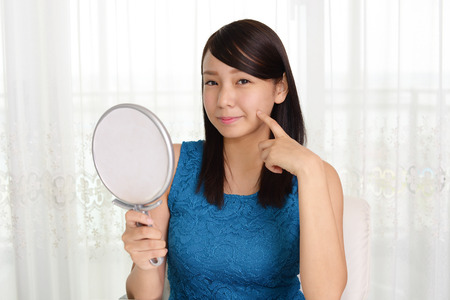 Asian woman looking at her face in mirrorの写真素材