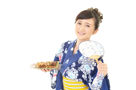 Smiling woman in Japanese summer kimono eating Yakitoriの写真素材