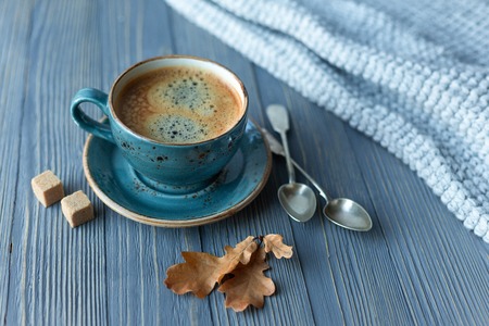 Blue cup whith coffee, knitted sweater, autumn leaves on wooden background. Cozy morning.の写真素材