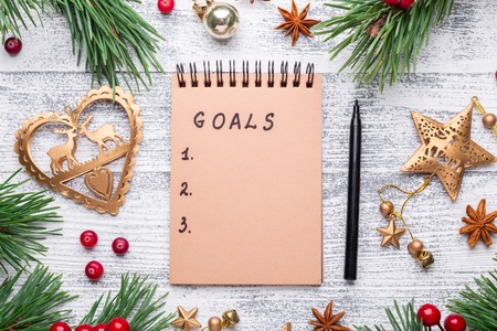 Fir branches, gifts and an notebook on a light wooden background. New goals. Cranberries, spices, holly berries. Christmas background. Flat lay, top view, copy space.の写真素材