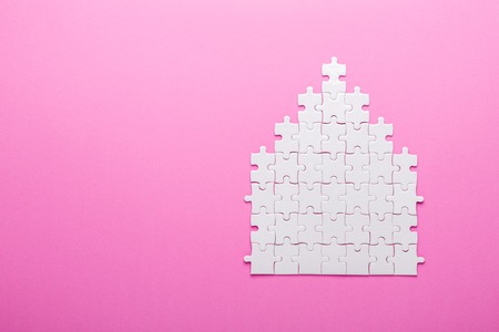 White puzzle. House shape puzzle. The concept of rent, mortgage. Pink background. Top view. Copy spaceの写真素材