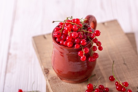 Fresh red currant in a ceramic cup on a white wooden background