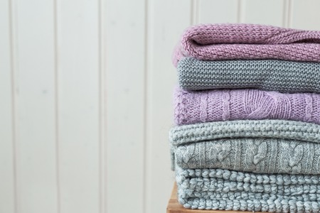 Stack of cozy knitted clothes on a wooden ladder. Scandinavian style. White wooden wall