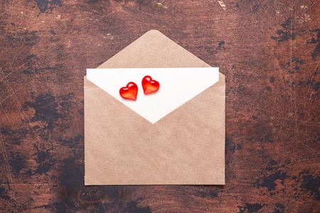 Craft envelope with red hearts on a vintage wooden background Piece of paper Valentine day concept Flat lay Top viewの写真素材