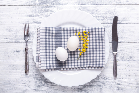 Easter table setting. White eggs, napkin on a plate, mimosa flowers, fork, knife on a wooden table. View from aboveの写真素材