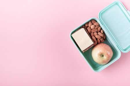 Lunch box with apple, sandwich and almond on pink background Back to school concept with copy space...