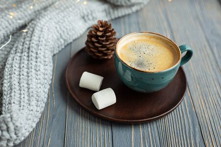 Cup of coffee, marshmallow, warm knitted sweater on wooden background. Warm lights. Cozy winter morning. Lifestyle concept. Selective focus.の写真素材