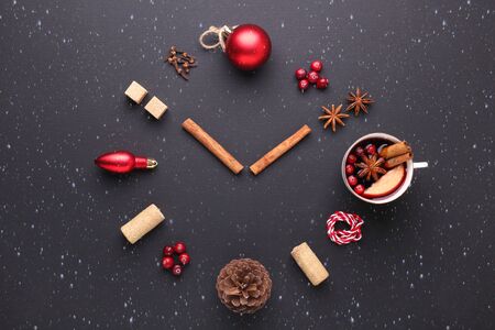 A clock in the form of spice for mulled wine. Cinnamon, anise stars, cranberries, brown sugar. Concept, creative work. Time to cook mulled wine. Snowfall drawing effect. Top view. Black backgroundの写真素材