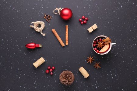 A clock in the form of spice for mulled wine. Cinnamon, anise stars, cranberries, brown sugar. Concept, creative work. Time to cook mulled wine. Snowfall drawing effect. Top view. Black backgroundの写真素材