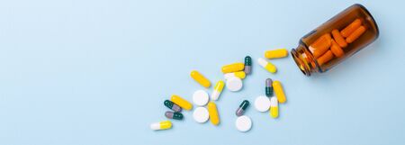 Multicolor tablets and pills capsules from glass bottle on blue background Heap of assorted various...