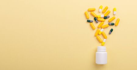 Multicolor tablets and pills capsules from plastic bottle on yellow background Health care...