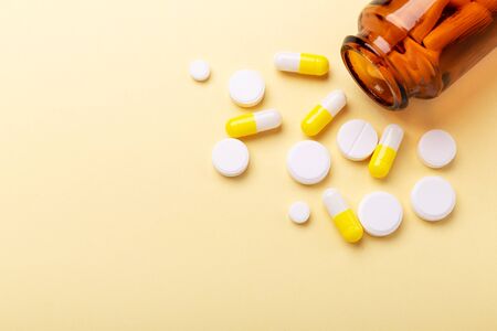 Multicolor tablets and pills capsules from glass bottle on yellow background Heap of assorted...