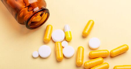 Multicolor tablets and pills capsules from glass bottle on yellow background Heap of assorted various medicine tablets and pills. Health care Close-up Copy spaceの写真素材