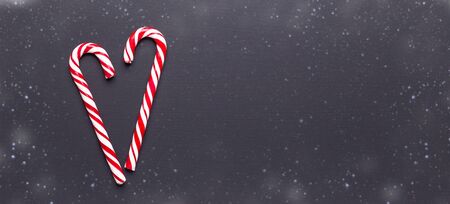 Two candy canes in shape of heart on black wooden background. Christmas, winter, new year concept....