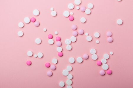 Pink and white pills on pink background. Heap of assorted various medicine tablets and pills. Health...